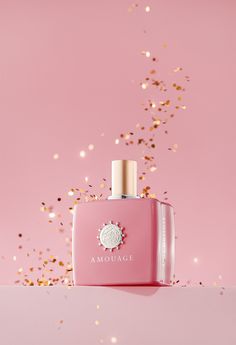 a bottle of amouage perfume on a pink background with gold confetti