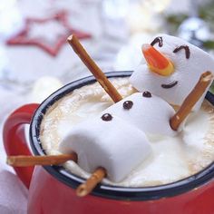 two marshmallow snowmen in a red mug with cinnamon sticks sticking out of it