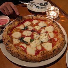 a pizza with mozzarella and spinach on it sitting on a white plate