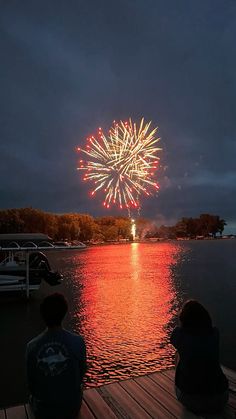 two people sitting on a dock watching fireworks