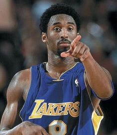 a basketball player pointing to the side with his hand on his hip and wearing a jersey that says lakers