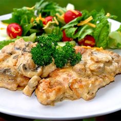 a white plate topped with meat covered in sauce and veggies next to a salad