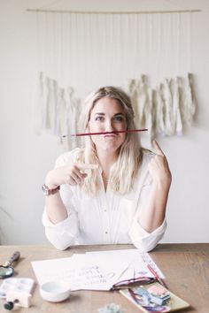 a woman sitting at a table with a pencil in her mouth