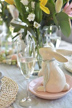 a table set for easter dinner with flowers in vases and bunny figurines