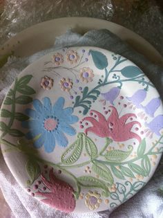 a plate with flowers painted on it sitting on top of a cloth covered tablecloth