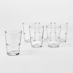 six glasses are lined up on a white surface, with one empty glass in the middle