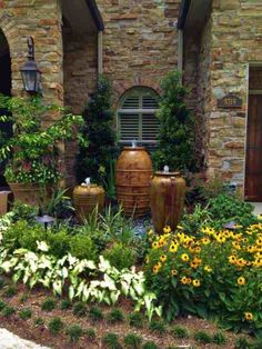 a garden with yellow flowers and large vases in front of a brick building on a sunny day