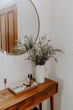 a wooden table topped with a white vase filled with flowers next to a round mirror