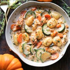 a white bowl filled with potatoes, zucchini and carrots on top of a wooden table