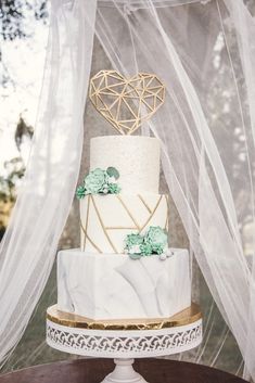 a white and gold wedding cake sitting on top of a table next to a net