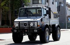 a silver truck driving down a street next to a tall building with lots of windows