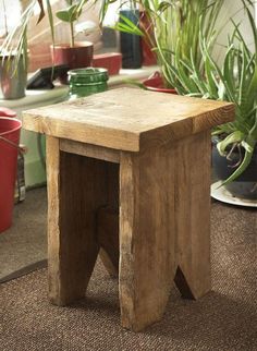 a wooden stool sitting on top of a carpeted floor next to potted plants