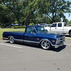 an old blue truck parked in a parking lot next to a white truck and trees