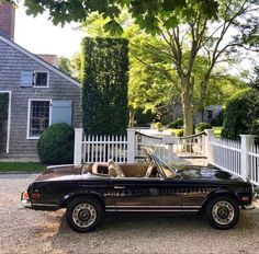 a black convertible car parked in front of a white picket fence with trees and houses behind it