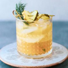 a close up of a drink in a glass on a plate with a rosemary garnish