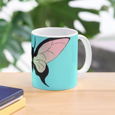 a coffee mug with a butterfly on it sitting on a table next to some books