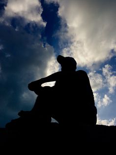 the silhouette of a man sitting against a cloudy sky