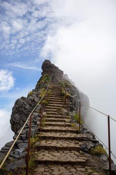 stairs leading up to the top of a mountain with clouds in the sky behind them