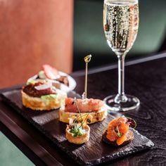 small appetizers and champagne are served on a wooden tray at a restaurant table