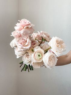 a person holding a bouquet of flowers in their hand with the background painted off white