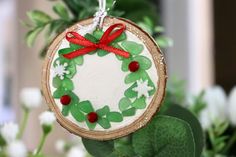 a christmas ornament hanging from a tree slice with green leaves and red ribbon