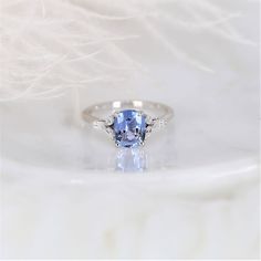 a ring with a blue stone in the center on a white tablecloth, next to some feathers