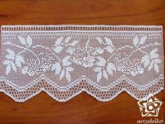 a white lace with flowers on it sitting on top of a wooden table next to a flower