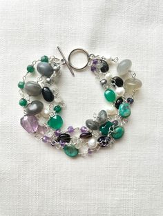 This multi-gemstone silver-plated wire-wrapped bracelet features gray moonstone, amethyst, labradorite, Smokey quartz, rainbow moonstone, green aventurine, green onyx, turquoise, iolite and freshwater pearls in a variety of shapes and sizes, set on 4 strands. This bracelet is 8 and 1/4 inches long and is finished with a 14 mm silver-plated toggle clasp.  This bracelet length can be altered to your specifications. These are genuine stones and may contain inclusions, and variations in size, color, Silver Circle Earrings, Wire Wrapped Bracelet, Multi Strand Bracelet, Labradorite Beads, Chakra Bracelet, Gold Plated Bracelets, Strand Bracelet, Green Amethyst, Green Onyx