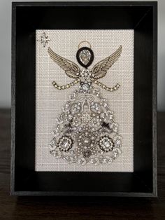 Sparkly angel meticulously handcrafted with rhinestone vintage jewelry. Presented on an ivory fabric background in a 5x7" shadow box like black frame. Unique piece can be hung on the wall or placed on a shelf, dresser, etc. Framed Jewelry Angel, Old Jewelry Repurposed, Old Jewelry Crafts Ideas, Shelf Dresser, Jewelry Angel