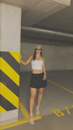 a woman standing next to a yellow and black striped pole in a parking garage area