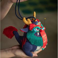 a hand holding a small stuffed animal with horns and tassels on it's head