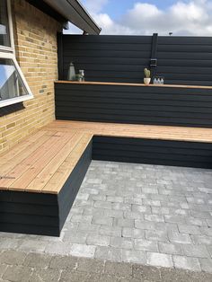 a wooden bench sitting in front of a brick wall next to a window on top of a building