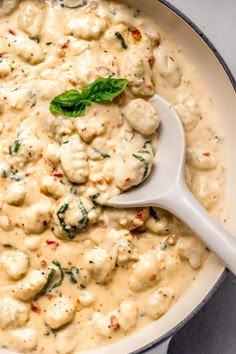 a white pot filled with macaroni and cheese covered in sauce, garnished with a green leaf