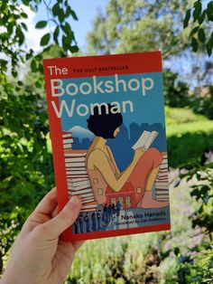 a person holding up a book in front of some trees and bushes with the title, bookshop woman