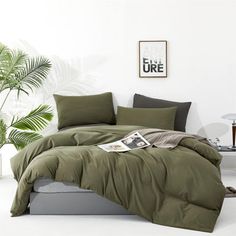 a bed with green sheets and pillows in a room next to a potted plant