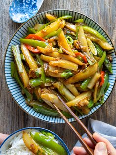 someone holding chopsticks over a bowl of stir fry with rice and green beans