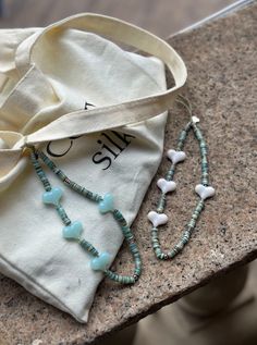 two necklaces and a bag sitting on top of a stone counter next to each other