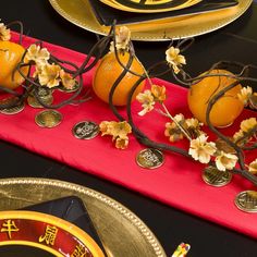 two oranges are sitting on a red table runner with gold plates and other decorations