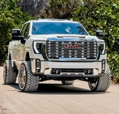 a white gmc truck driving down a road next to some bushes and trees in the background