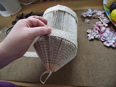 a person is holding a paper fan on a table with flowers and other items in the background