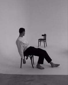 a black and white photo of a man sitting on a chair in front of two chairs