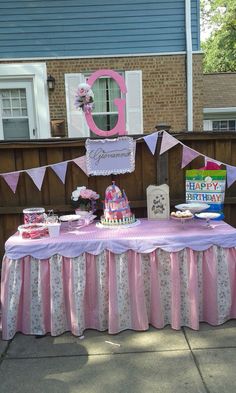 a pink and white table topped with cake next to a wooden fence in front of a house