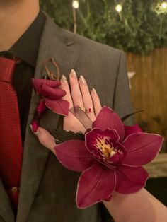 a man in a suit and red tie holding a flower with his hand on the woman's wrist