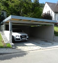 a white car parked in a garage on the side of a road next to a house