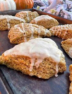 there are several scones with icing on the baking sheet and pumpkins in the background