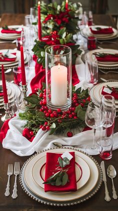 the table is set for christmas dinner with red napkins and greenery