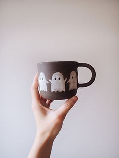 a hand holding a coffee cup with three ghost on it