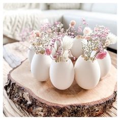 four eggs with flowers in them sitting on a wooden table next to a white couch