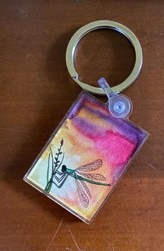 a keychain with a dragonfly on it sitting on top of a wooden table