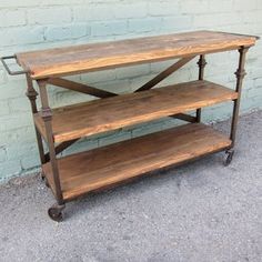 a wooden table sitting next to a brick wall on top of a cement floor with wheels